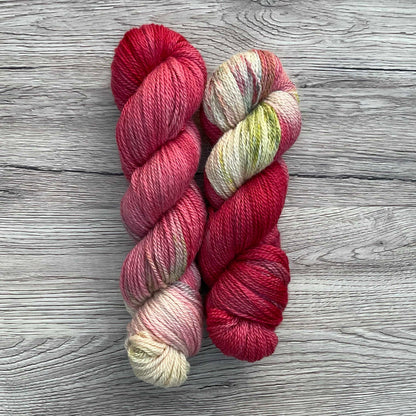 Two skeins of yarn on a wood effect background. The yarn is predominantly red with a speckled cream end.