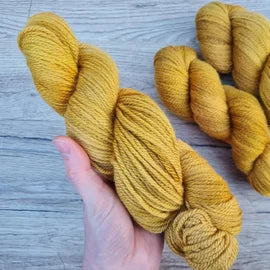 A white hand holds a skein of warm golden yarn.