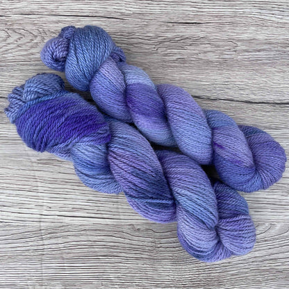 Two skeins of purple yarn on a wood effect background.