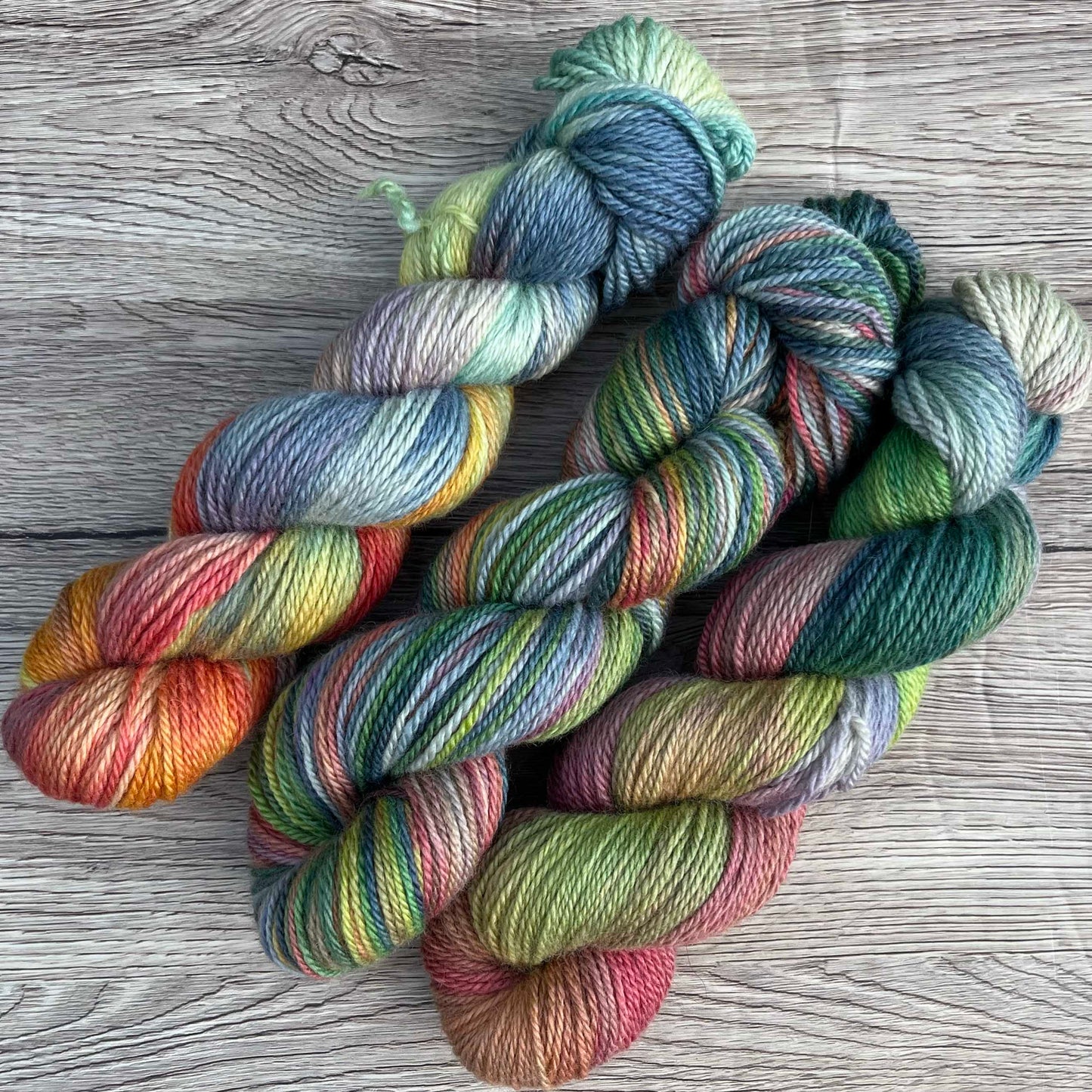 Three skeins of rainbow yarn diagonally across the photo, on a wood effect background.