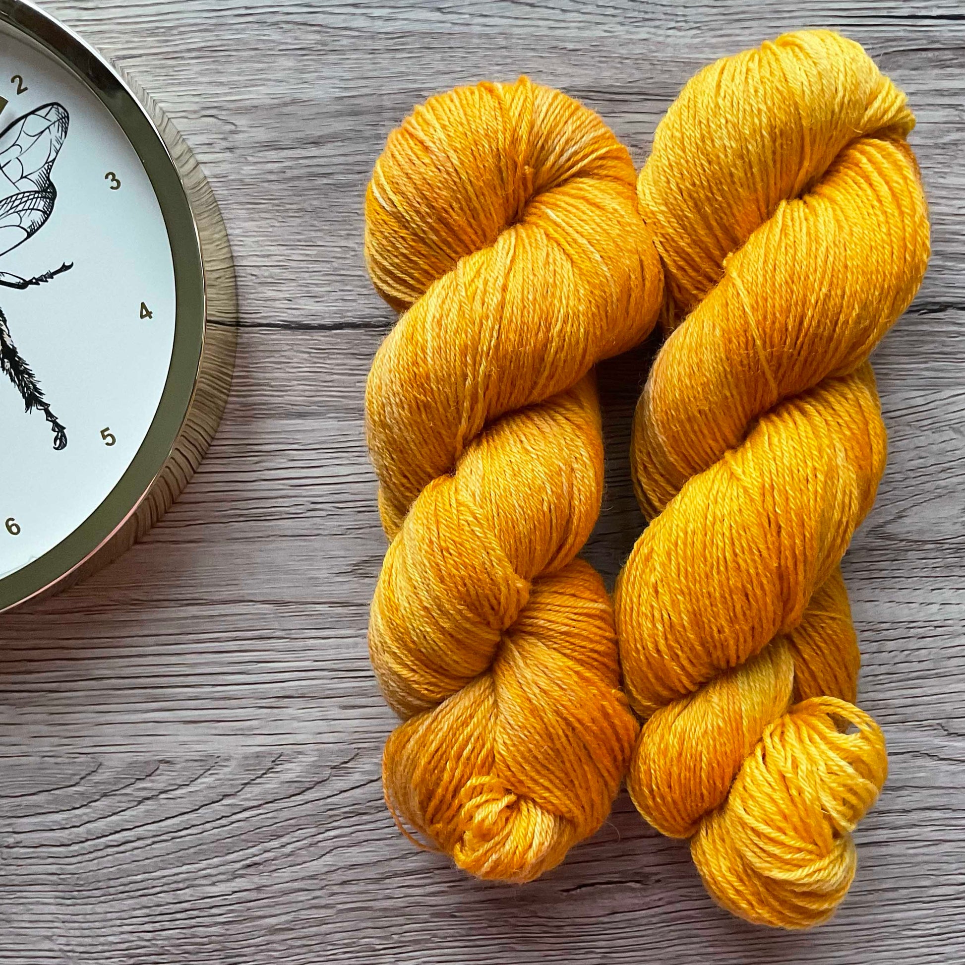 Two skeins of warm golden yarn on a wood effect background.