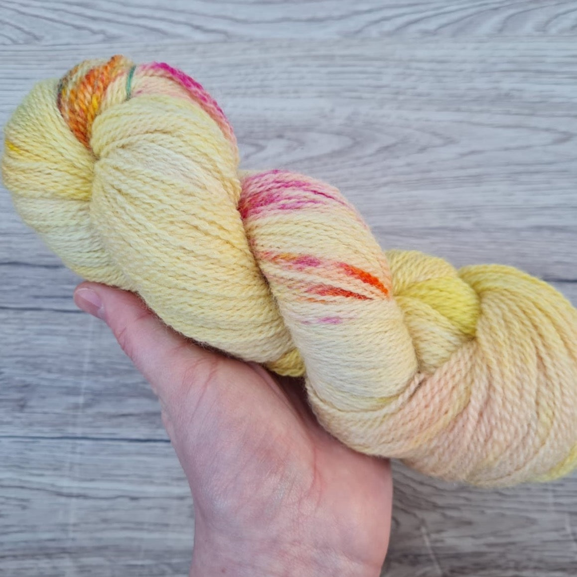 A hand holding a skein of speckled yellow yarn.