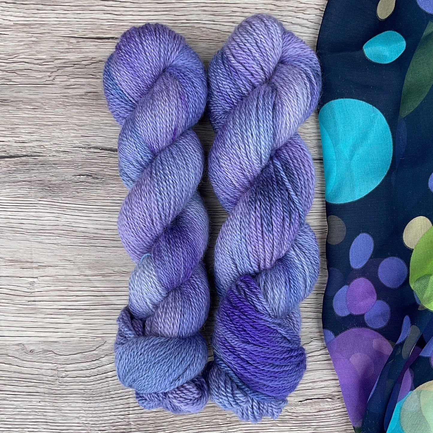 Two skeins of purple yarn beside a complimentary fabric on a wood background.