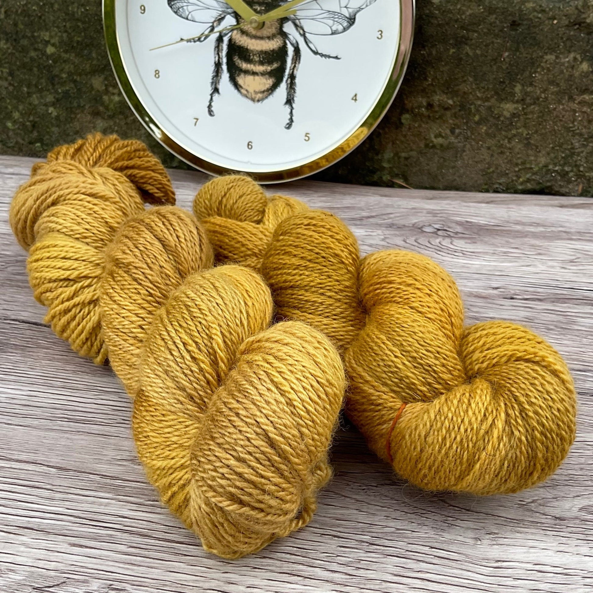 Two skeins of warm golden yarn in front of a bee clock.