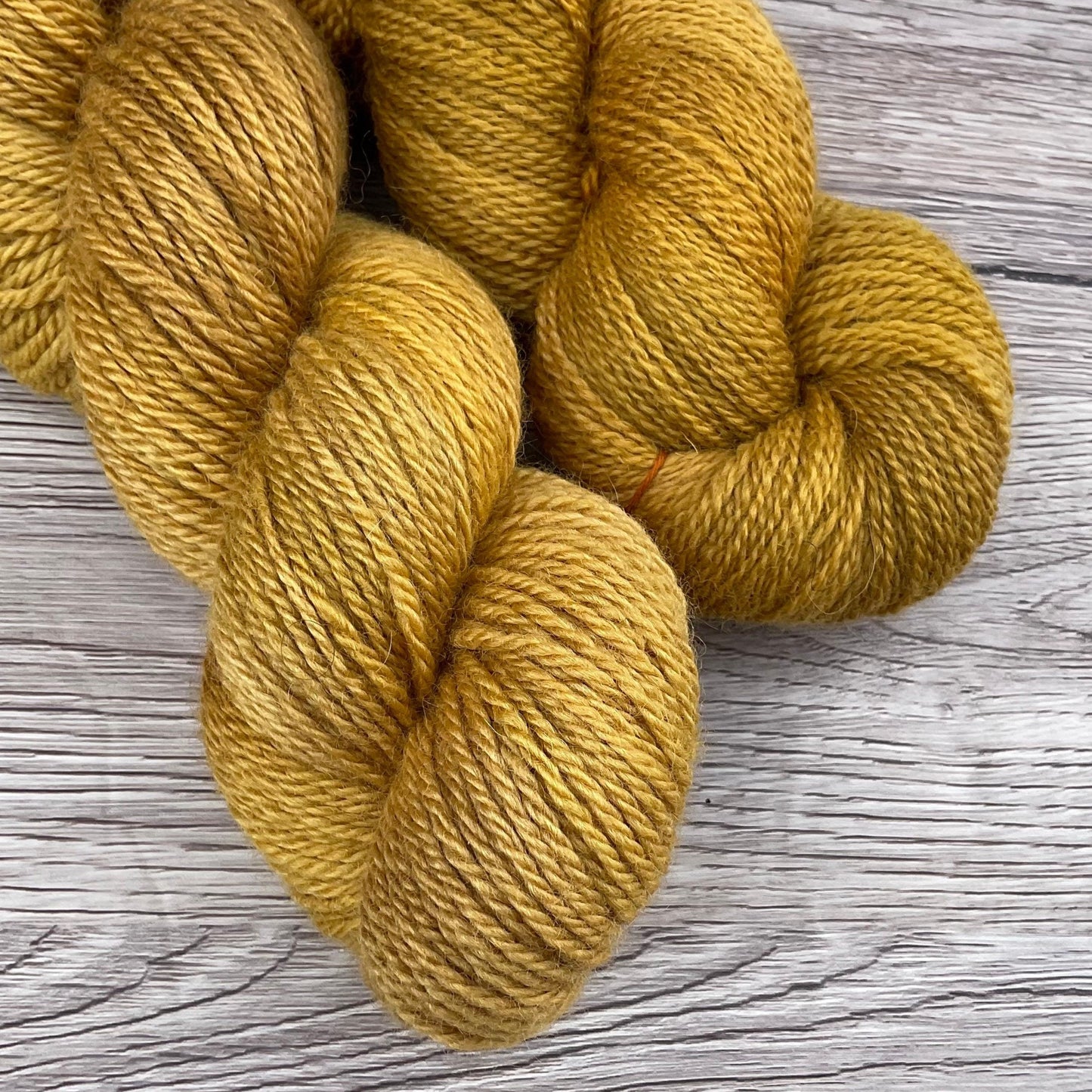 A close up of two skeins of warm golden yarn on a wood effect background.