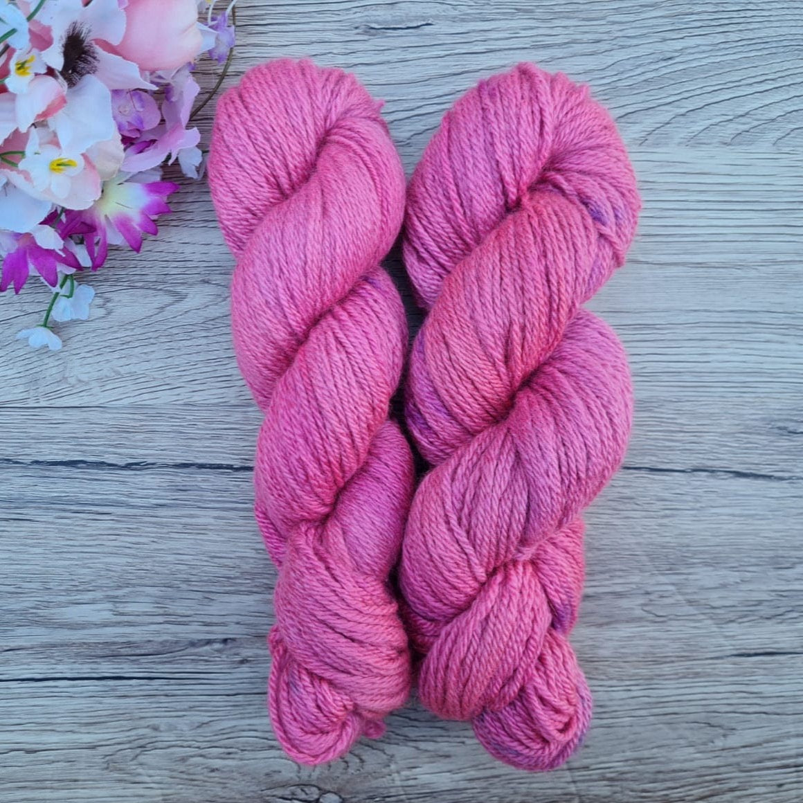 Two skeins of pink tonal yarn on a wood effect background with flowers.