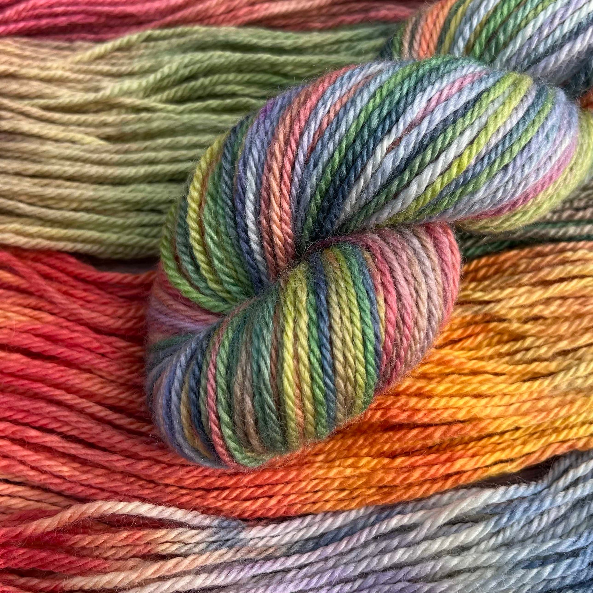 A skein of rainbow yarn peeks into the photo. The background is the same colourway.